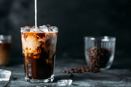 Cold brew in a glass with ice as milk is poured in, creating swirls